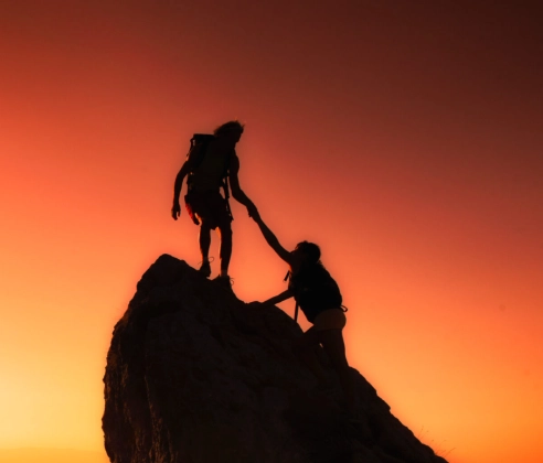 Silhouettes of a man and woman climbing a mountain